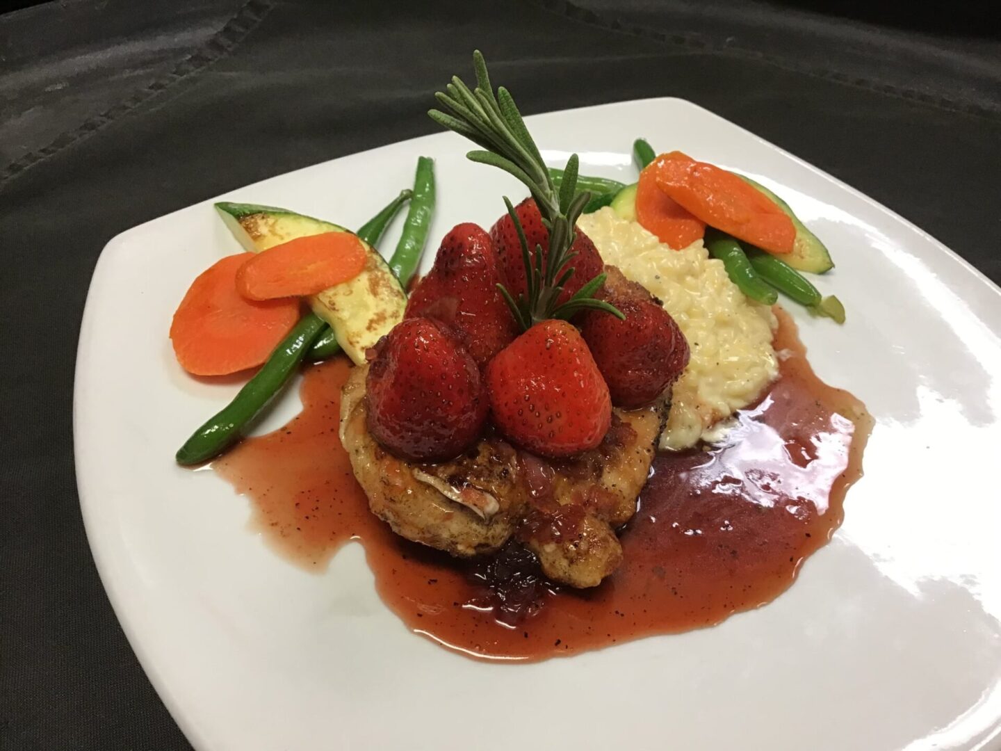 Plated meat dish with garnished with strawberries, carrots, string beans, and topped with a sauce