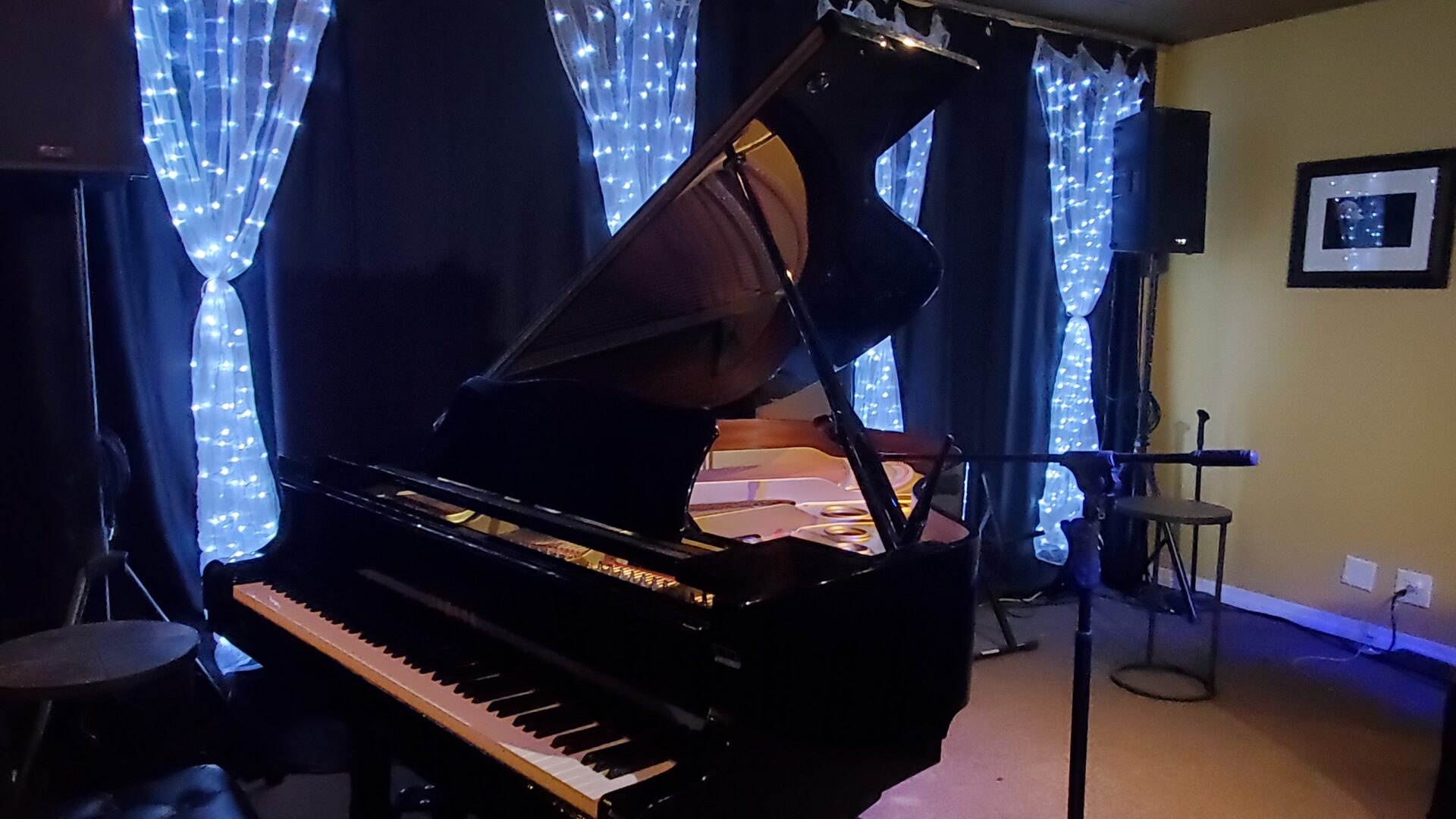 Black grand piano in front of white pulled curtains illuminated by fairy lights