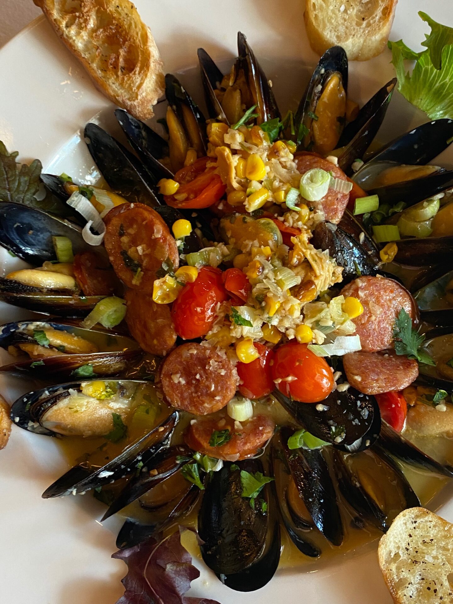 Platter of mussels with corn and tomato garnishing and slices of bread as a side dish
