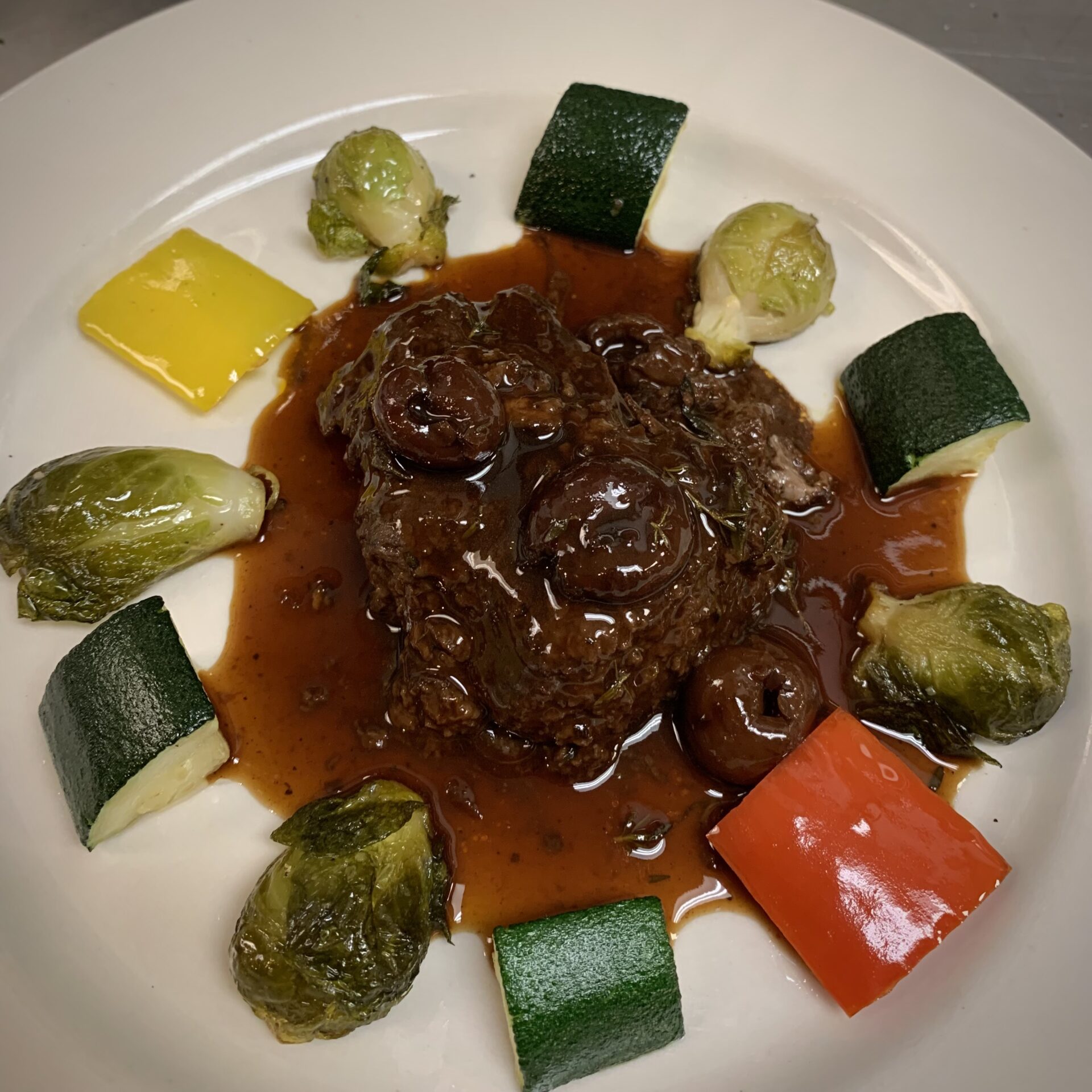 Platted main course dish with a brown sauce and garnished with cucumbers and brussels sprouts.